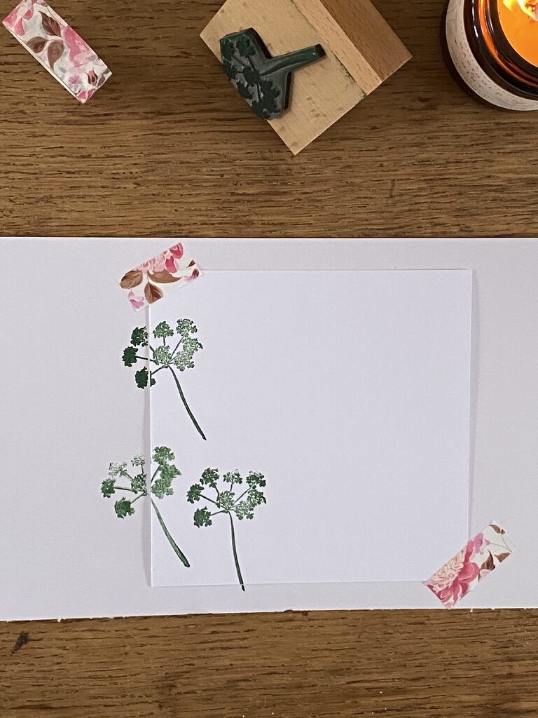 rubber stamp design of cow parsley onto paper secured with washi tape with candle and craft stamp in background