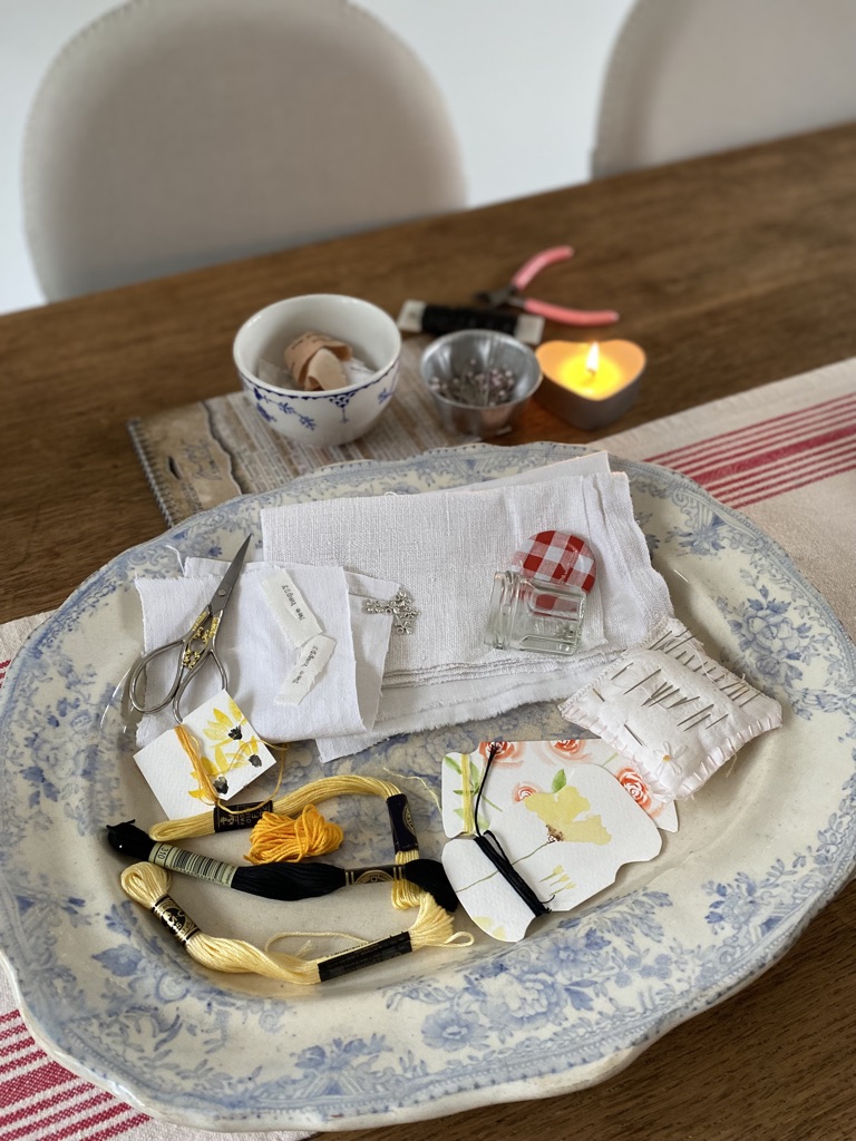 variety of craft materials on top of blue and white plate including embroidery threads scissors needles and vintage fabrics