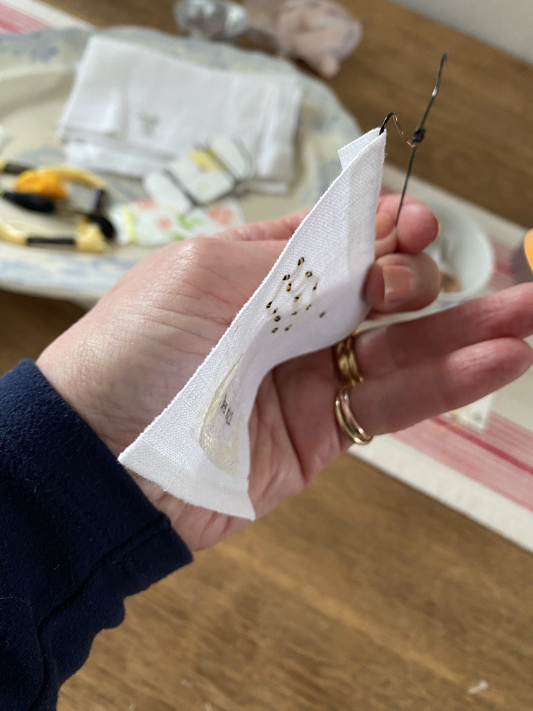 hand holds embroidered piece showing how to sew and secure to mini craft wire hanger