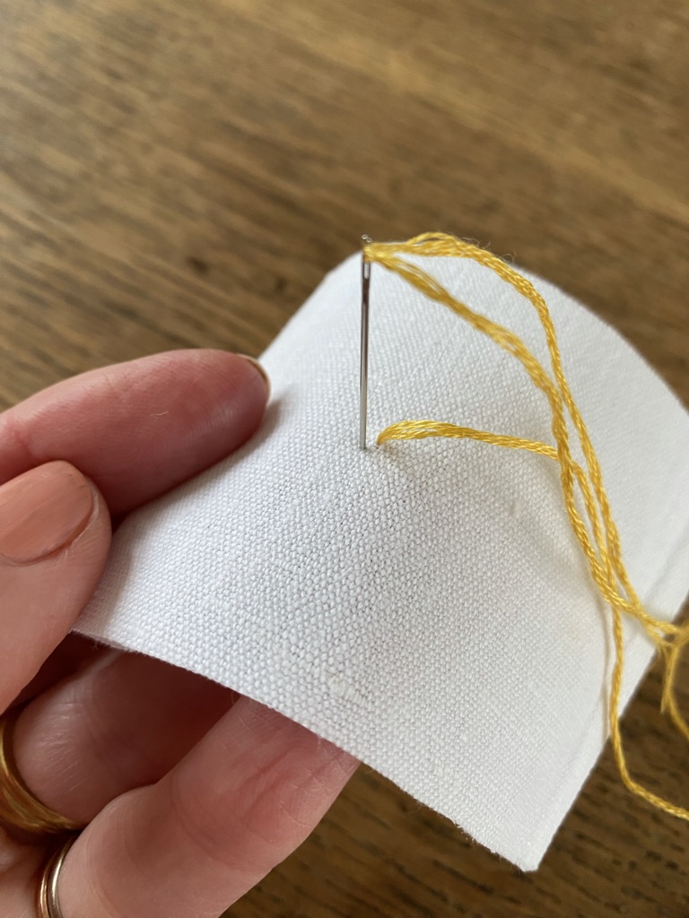 hand sewing yellow thread through white linen