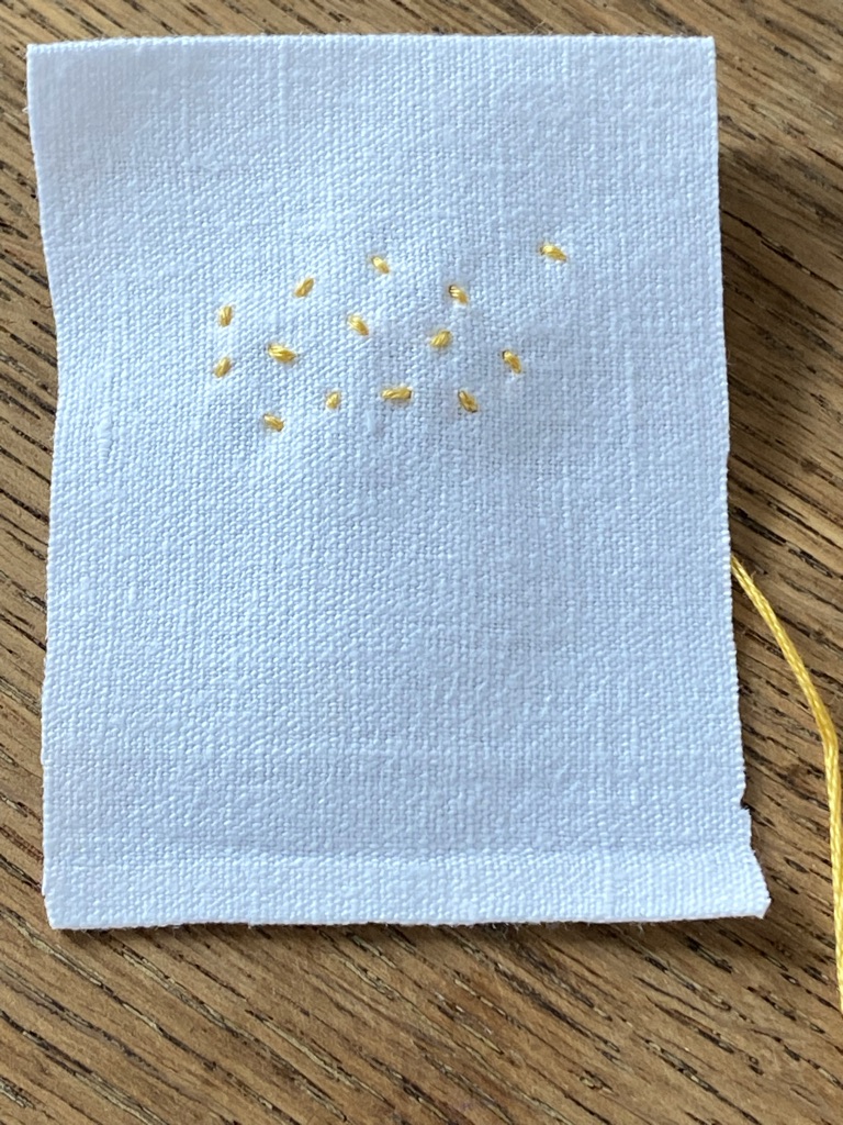 number of small yellow stab stitches dotted around piece of vintage white linen