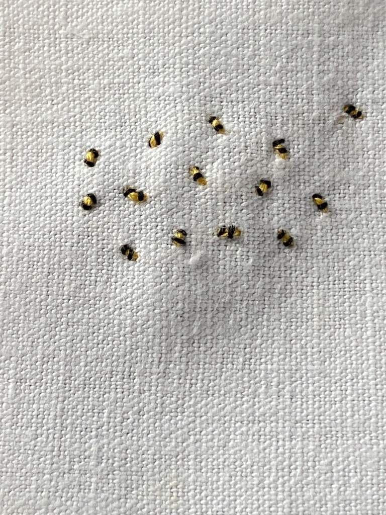 tiny stitches create a simple bumble bee embroidery on white linen