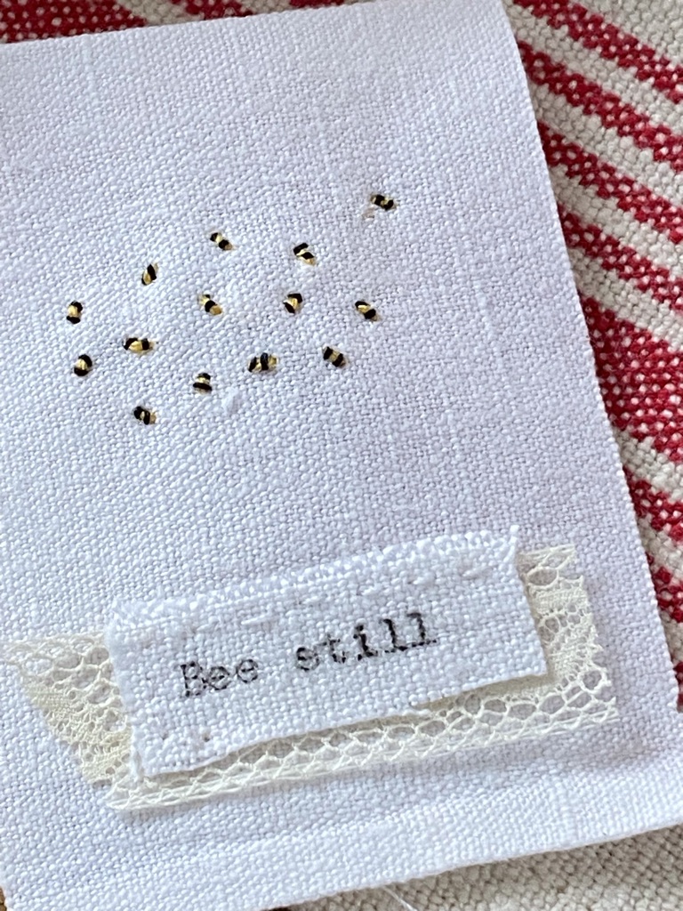 a colony of embroidered yellow and black tiny bumble bees and type written words Bee Still added on top of scrap of lace