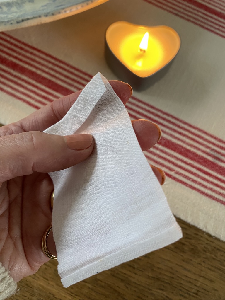 female hand holding white linen next to a heart shaped candle ontop of red and cream striped table runner